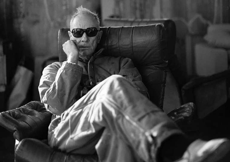 Black-and-white promotional portrait of DJ Driller wearing sunglasses while lounging back in a leather armchair.